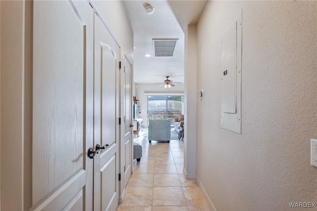 corridor with light tile patterned floors, a textured wall, visible vents, and baseboards