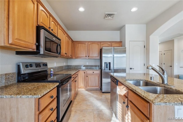 kitchen featuring visible vents, appliances with stainless steel finishes, a kitchen island with sink, a sink, and light stone countertops