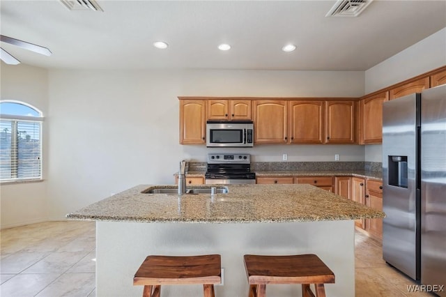 kitchen with visible vents, appliances with stainless steel finishes, light stone countertops, a kitchen bar, and a sink