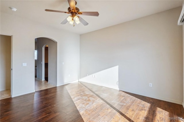 empty room with a ceiling fan, baseboards, arched walkways, and wood finished floors