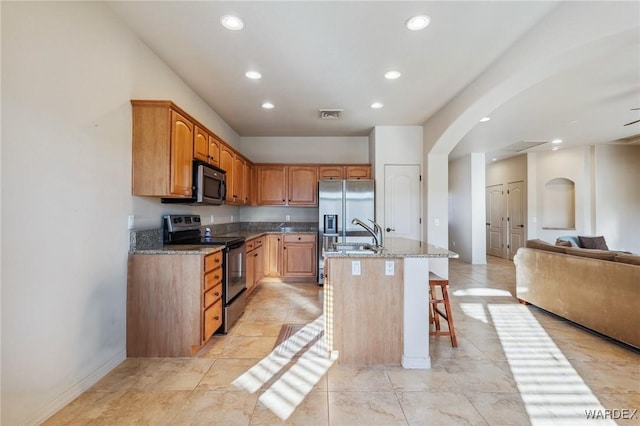 kitchen featuring stainless steel appliances, visible vents, open floor plan, a sink, and an island with sink