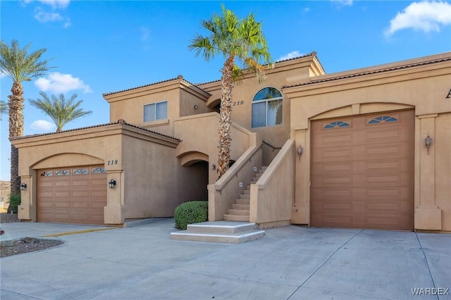 mediterranean / spanish-style home with a garage, concrete driveway, a tiled roof, and stucco siding