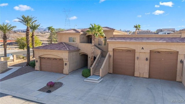 mediterranean / spanish home with stucco siding, stairway, a garage, driveway, and a tiled roof