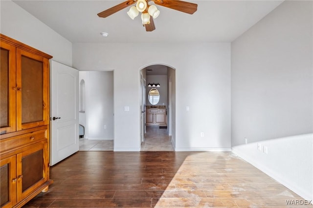 unfurnished room featuring a ceiling fan, arched walkways, baseboards, and wood finished floors