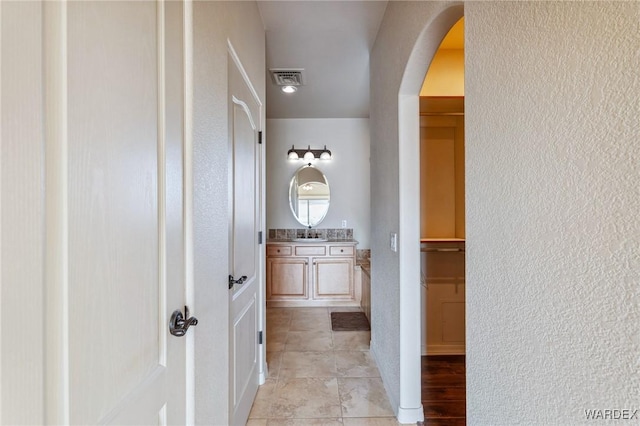 hallway featuring arched walkways, light tile patterned floors, visible vents, a textured wall, and a sink