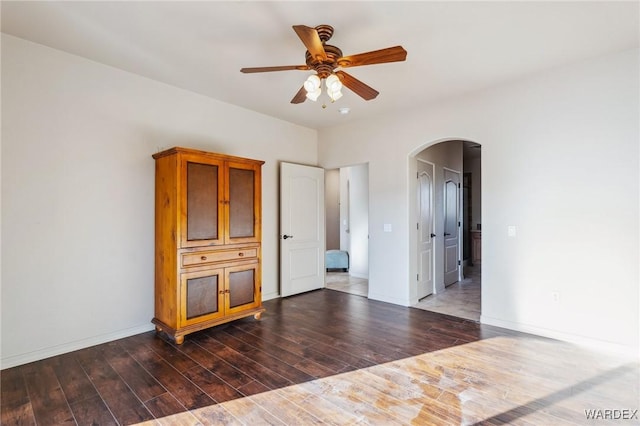 unfurnished room featuring a ceiling fan, arched walkways, dark wood-style flooring, and baseboards