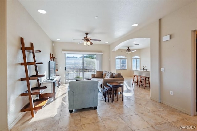 living room featuring arched walkways, ceiling fan, light tile patterned floors, recessed lighting, and baseboards