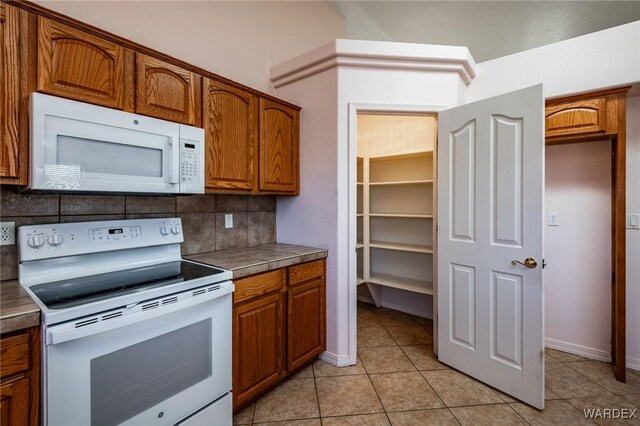 kitchen featuring tile countertops, light tile patterned floors, white appliances, tasteful backsplash, and brown cabinetry