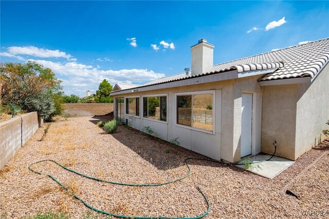 back of property featuring stucco siding, a fenced backyard, a chimney, and a tiled roof