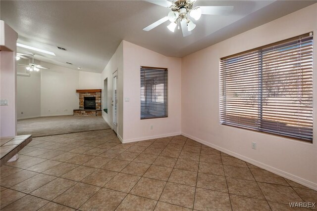 tiled empty room with lofted ceiling, visible vents, a ceiling fan, a stone fireplace, and baseboards