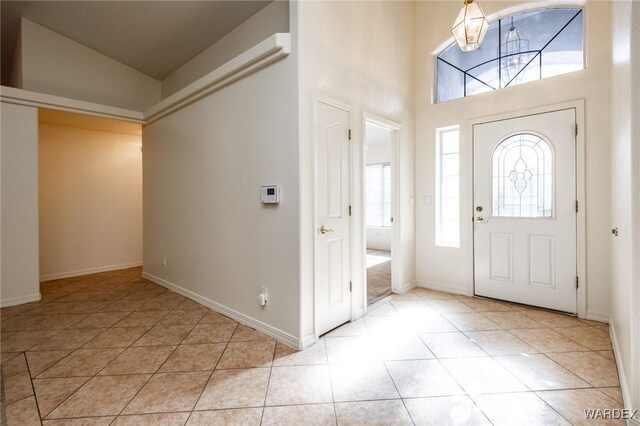 entrance foyer featuring a chandelier, high vaulted ceiling, light tile patterned flooring, and baseboards