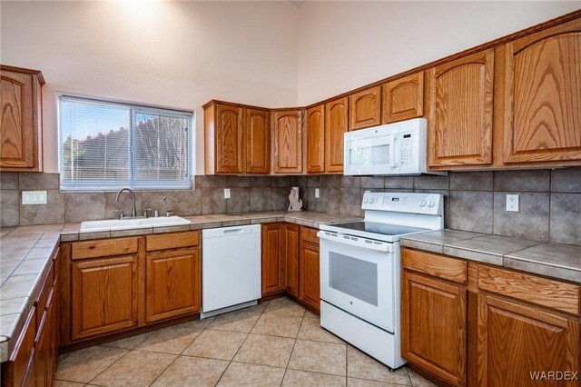 kitchen with tile countertops, white appliances, brown cabinets, and a sink