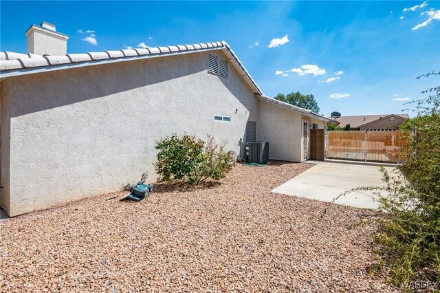 view of home's exterior featuring central air condition unit, fence, a gate, stucco siding, and a patio area