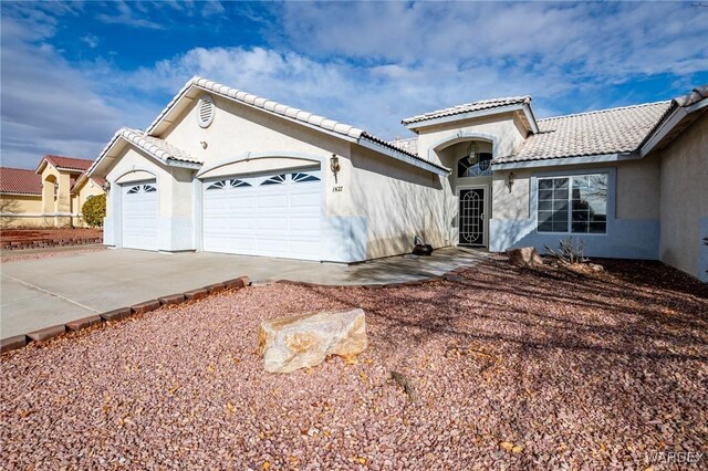 mediterranean / spanish-style house with an attached garage, a tiled roof, concrete driveway, and stucco siding