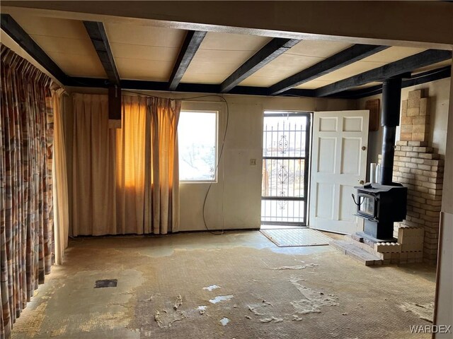 unfurnished living room with beamed ceiling and a wood stove