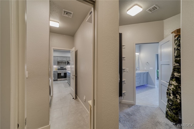 hallway featuring baseboards, visible vents, a textured wall, and light carpet