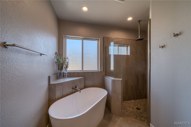 bathroom with a soaking tub, a walk in shower, and a textured wall