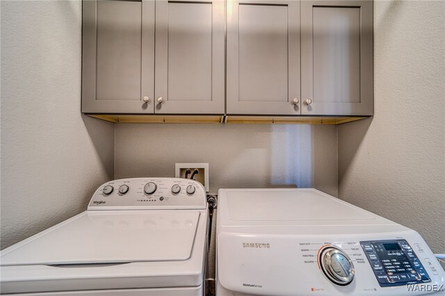 laundry area featuring a textured wall, cabinet space, and washing machine and clothes dryer