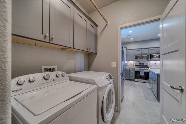 clothes washing area with visible vents, washer and dryer, cabinet space, light tile patterned flooring, and a textured wall