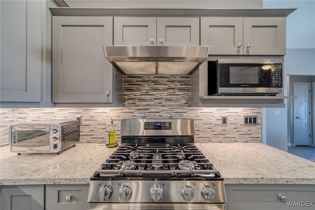 kitchen with under cabinet range hood, appliances with stainless steel finishes, tasteful backsplash, and gray cabinetry