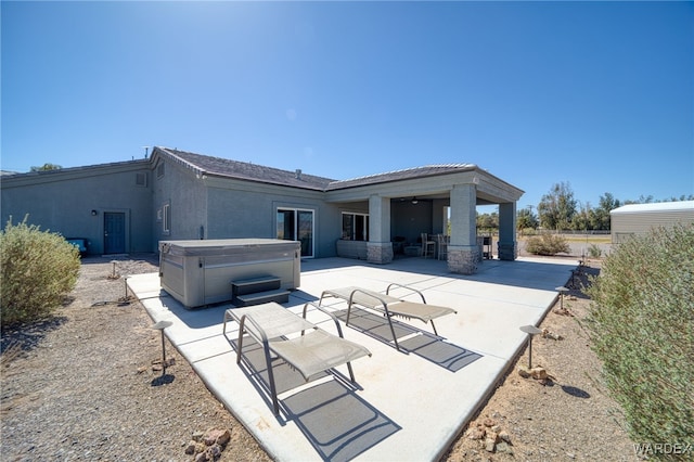 back of property featuring stucco siding, a patio, and a hot tub