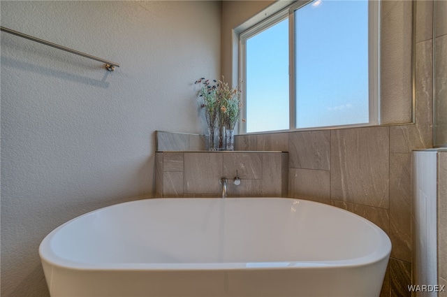 full bathroom featuring a soaking tub and a textured wall