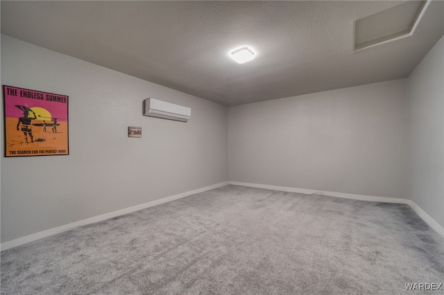 carpeted spare room featuring a wall unit AC, baseboards, and a textured ceiling