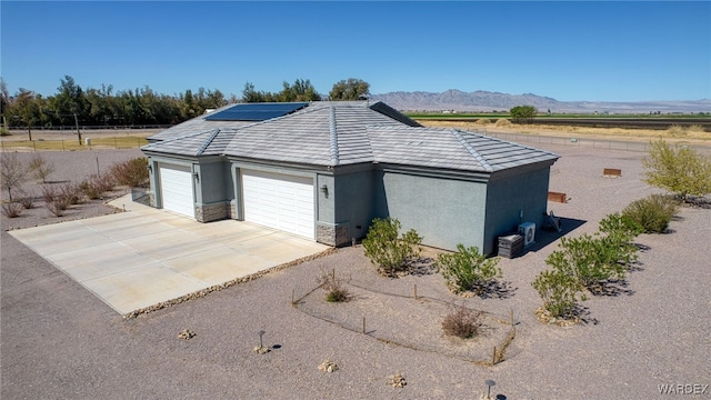 view of side of home with an attached garage, concrete driveway, stone siding, a mountain view, and roof mounted solar panels