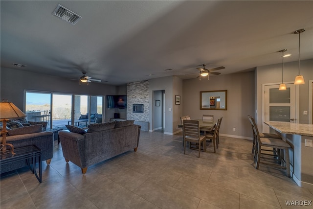 living area with a stone fireplace, baseboards, visible vents, and ceiling fan