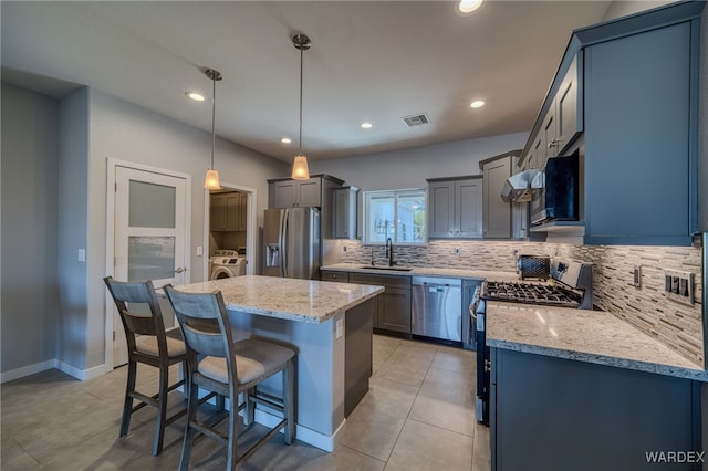 kitchen featuring visible vents, light stone countertops, a kitchen bar, stainless steel appliances, and a sink