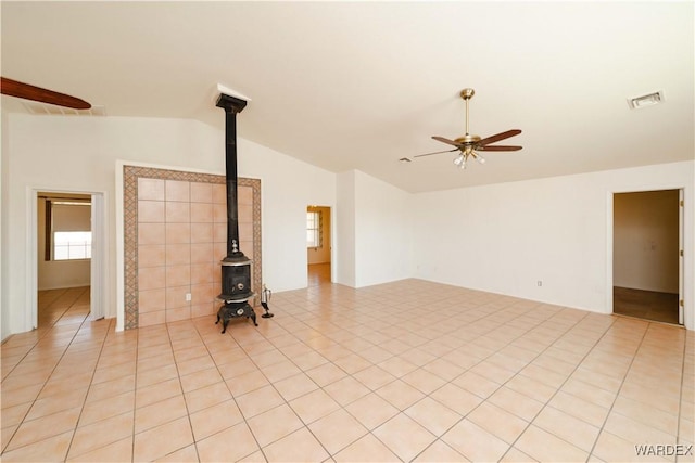 unfurnished living room featuring lofted ceiling, a wood stove, visible vents, a wealth of natural light, and ceiling fan