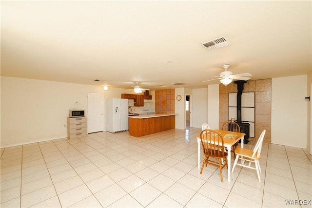 kitchen featuring a wood stove, white refrigerator with ice dispenser, ceiling fan, and visible vents
