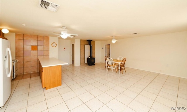 kitchen with light countertops, a wood stove, visible vents, white fridge with ice dispenser, and ceiling fan