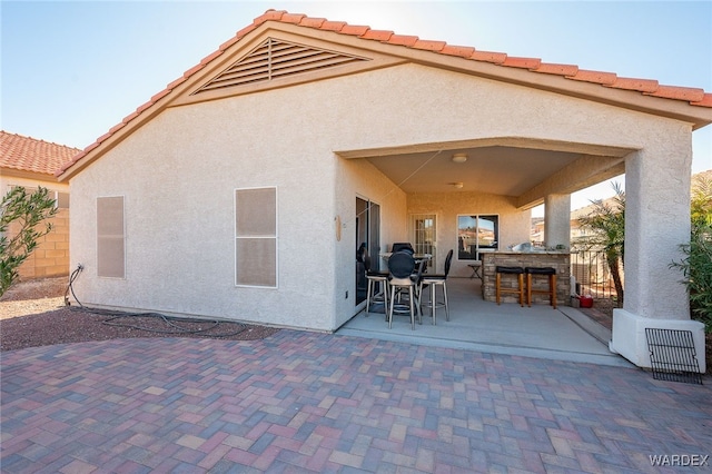 rear view of house featuring stucco siding, a tiled roof, outdoor dry bar, and a patio