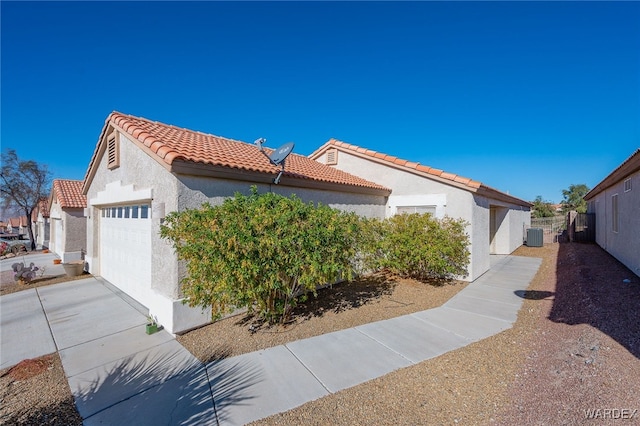 view of property exterior with concrete driveway, a tiled roof, an attached garage, central air condition unit, and stucco siding