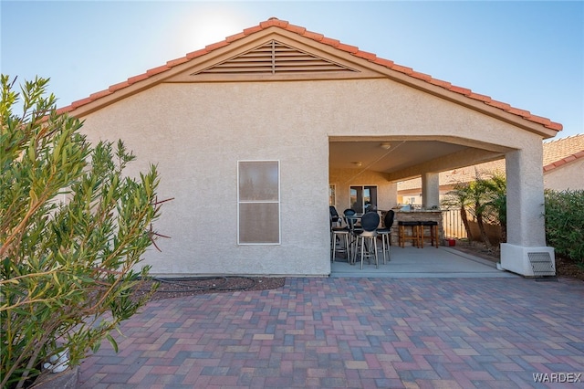 rear view of house featuring exterior bar, a patio area, a tile roof, and stucco siding