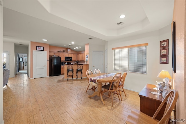 dining room with light wood-type flooring, a raised ceiling, visible vents, and baseboards