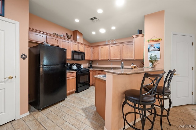 kitchen with light wood finished floors, visible vents, a peninsula, black appliances, and a kitchen bar