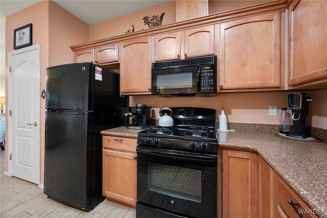 kitchen with dark countertops, light wood-style flooring, black appliances, and light brown cabinetry