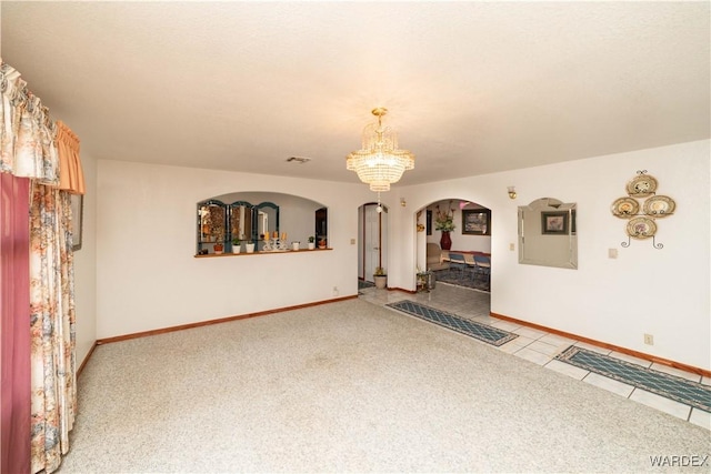 empty room with light tile patterned floors, baseboards, visible vents, arched walkways, and a notable chandelier