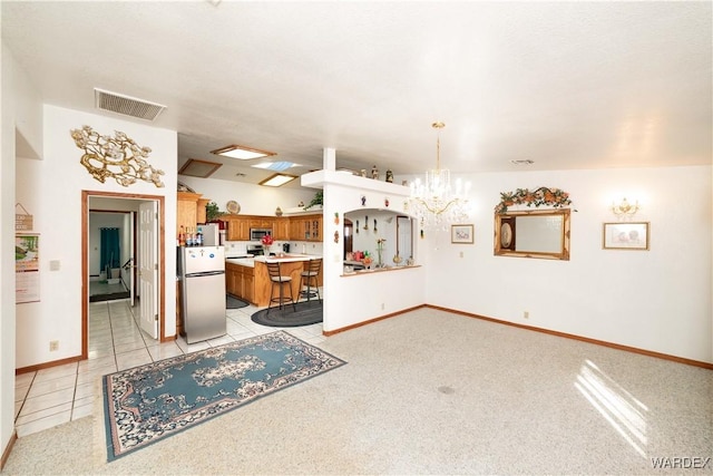 kitchen featuring visible vents, brown cabinets, a breakfast bar, freestanding refrigerator, and hanging light fixtures