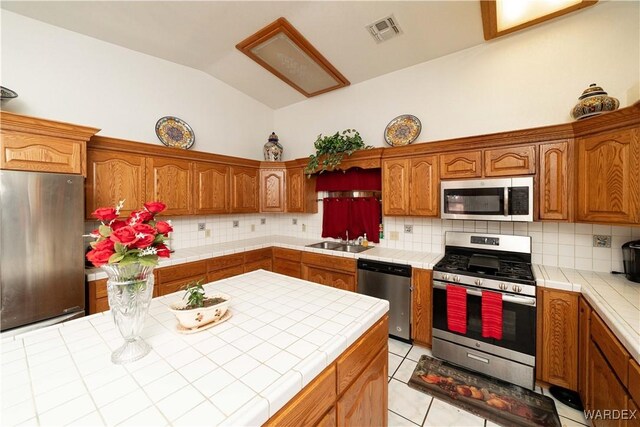 kitchen with stainless steel appliances, tile counters, visible vents, vaulted ceiling, and a sink