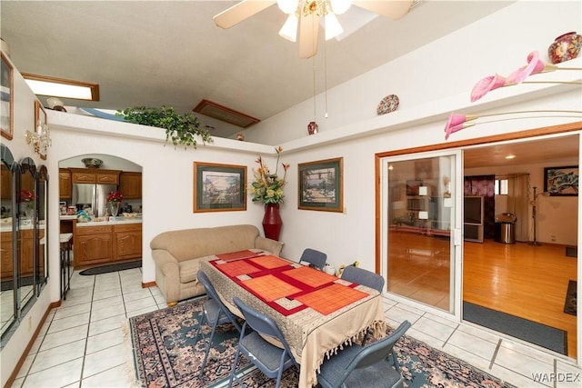 dining room featuring ceiling fan, arched walkways, vaulted ceiling, and light tile patterned floors