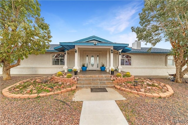 view of exterior entry featuring a porch, a chimney, and stucco siding