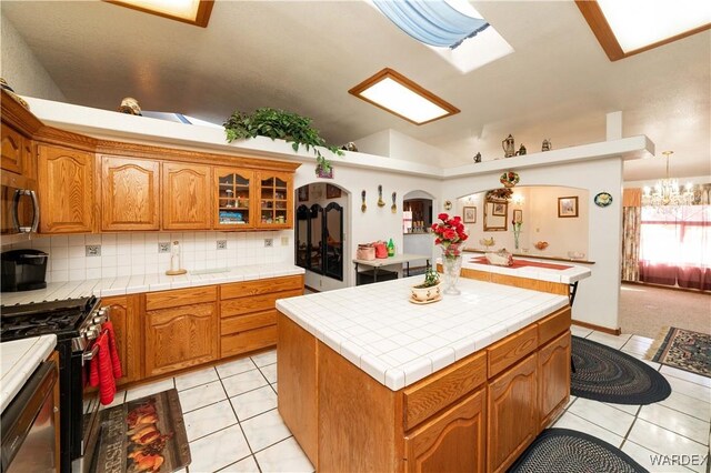 kitchen with tile countertops, light tile patterned floors, stainless steel appliances, a kitchen island, and glass insert cabinets