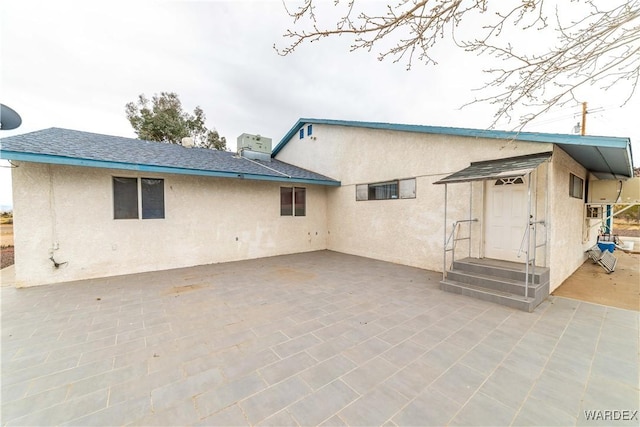 back of property with a shingled roof, a patio area, and stucco siding