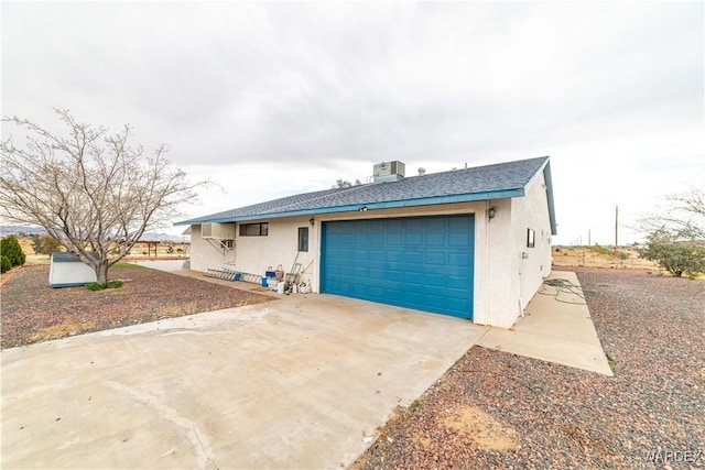 view of front of house featuring a garage, concrete driveway, central air condition unit, and stucco siding