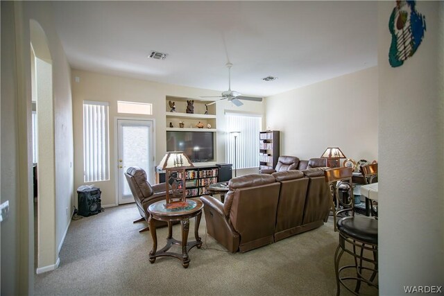 carpeted living area with ceiling fan, built in features, visible vents, and baseboards