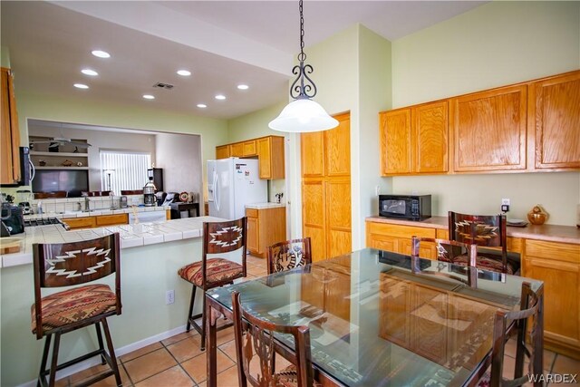 kitchen with brown cabinets, tile counters, visible vents, white fridge with ice dispenser, and black microwave