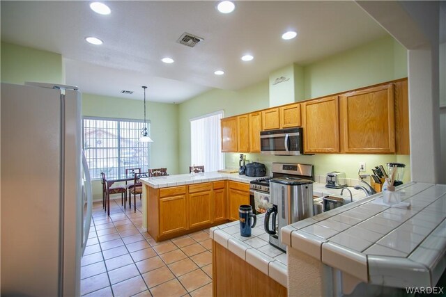 kitchen with tile countertops, stainless steel appliances, a peninsula, visible vents, and pendant lighting